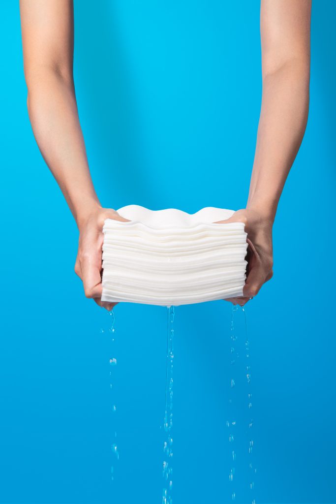 Khăn ướt Hoppi Daily Cleanse chứa nhiều nước 3.5x water được vắt nước trực tiếp bằng tay trên nền xanh